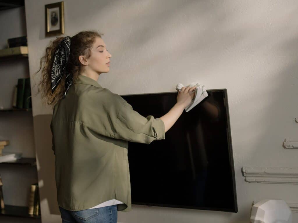 Woman in Gray Long Sleeve Shirt and Blue Denim Jeans Standing Near Black Flat Screen Tv